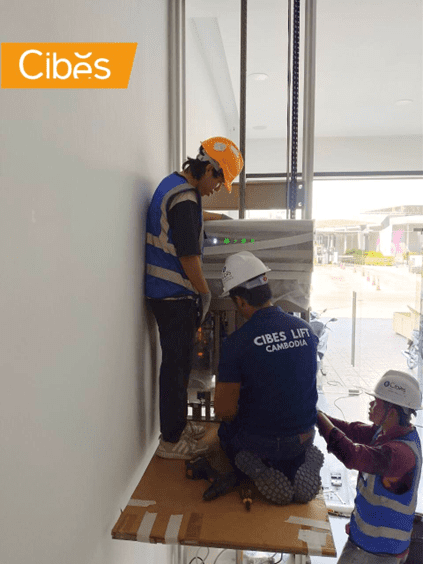 ជាងបច្ចេកទេស Cibes Lift Cambodia កំពុងតម្លើងជណ្តើរយន្តក្នុងផ្ទះ។